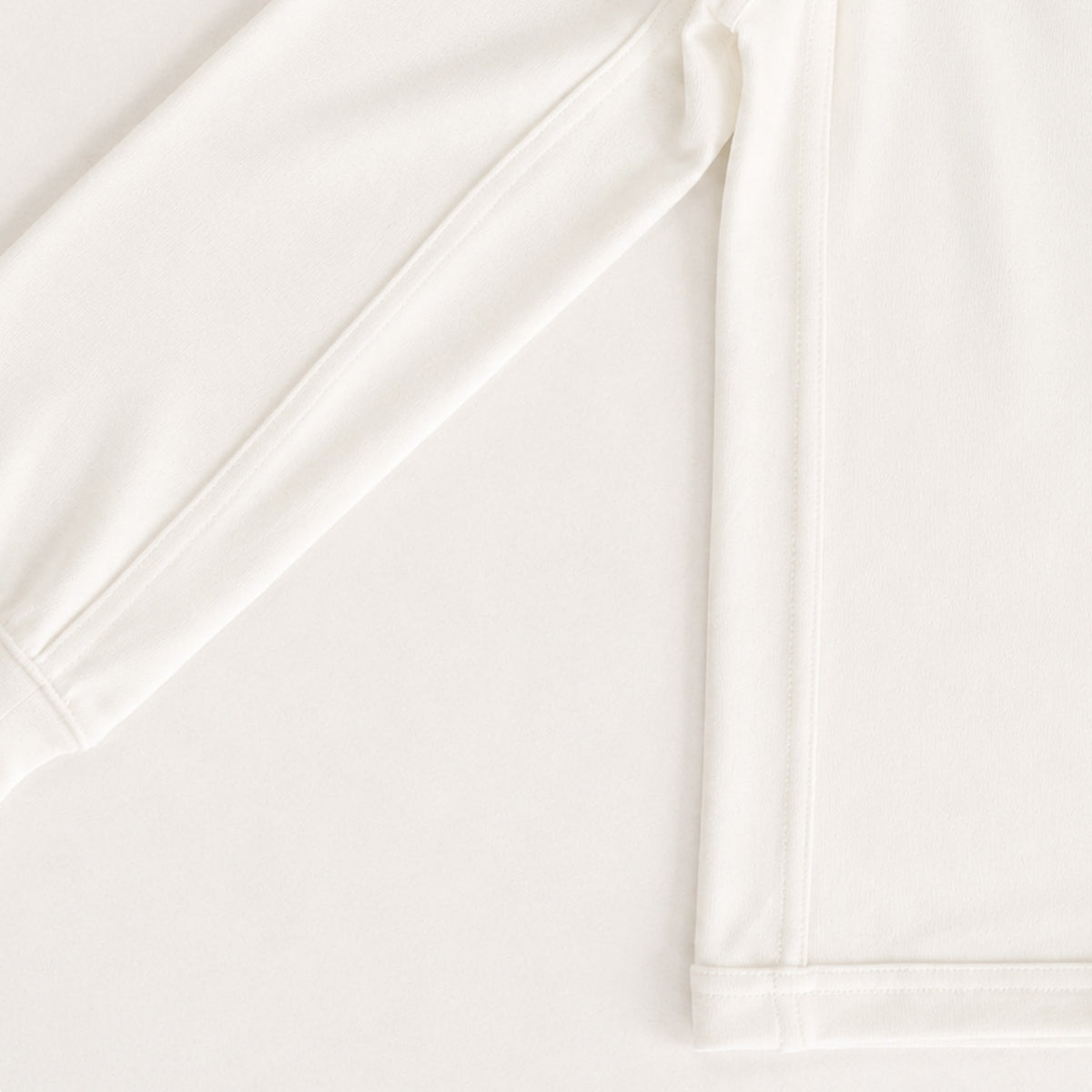 Close-up of a plain white long-sleeve garment showing the sleeve cuff and hem with clean stitching.
