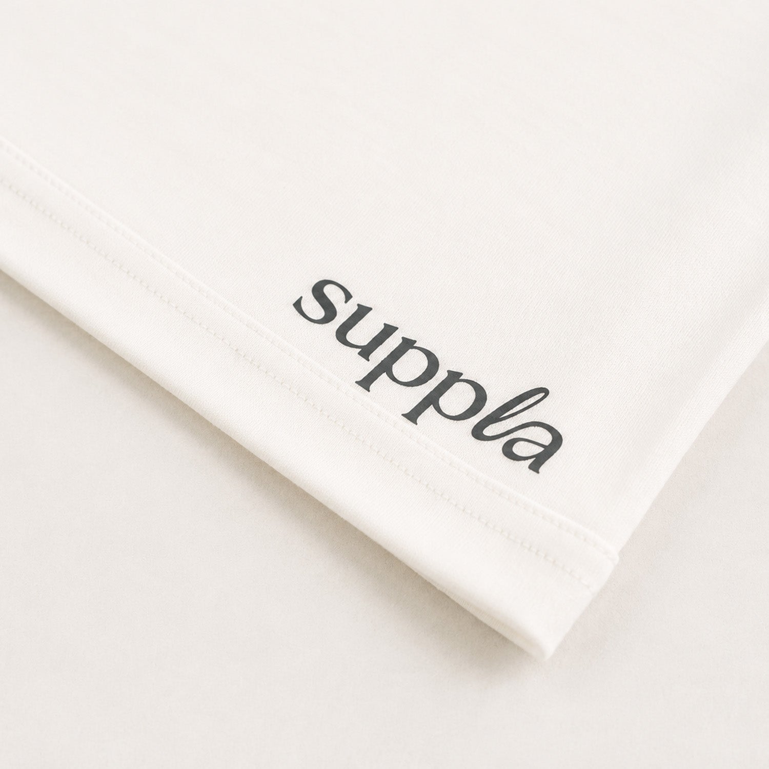 A close-up of a white tshirt featuring the brand name 'suppla' printed in black script near the hem.