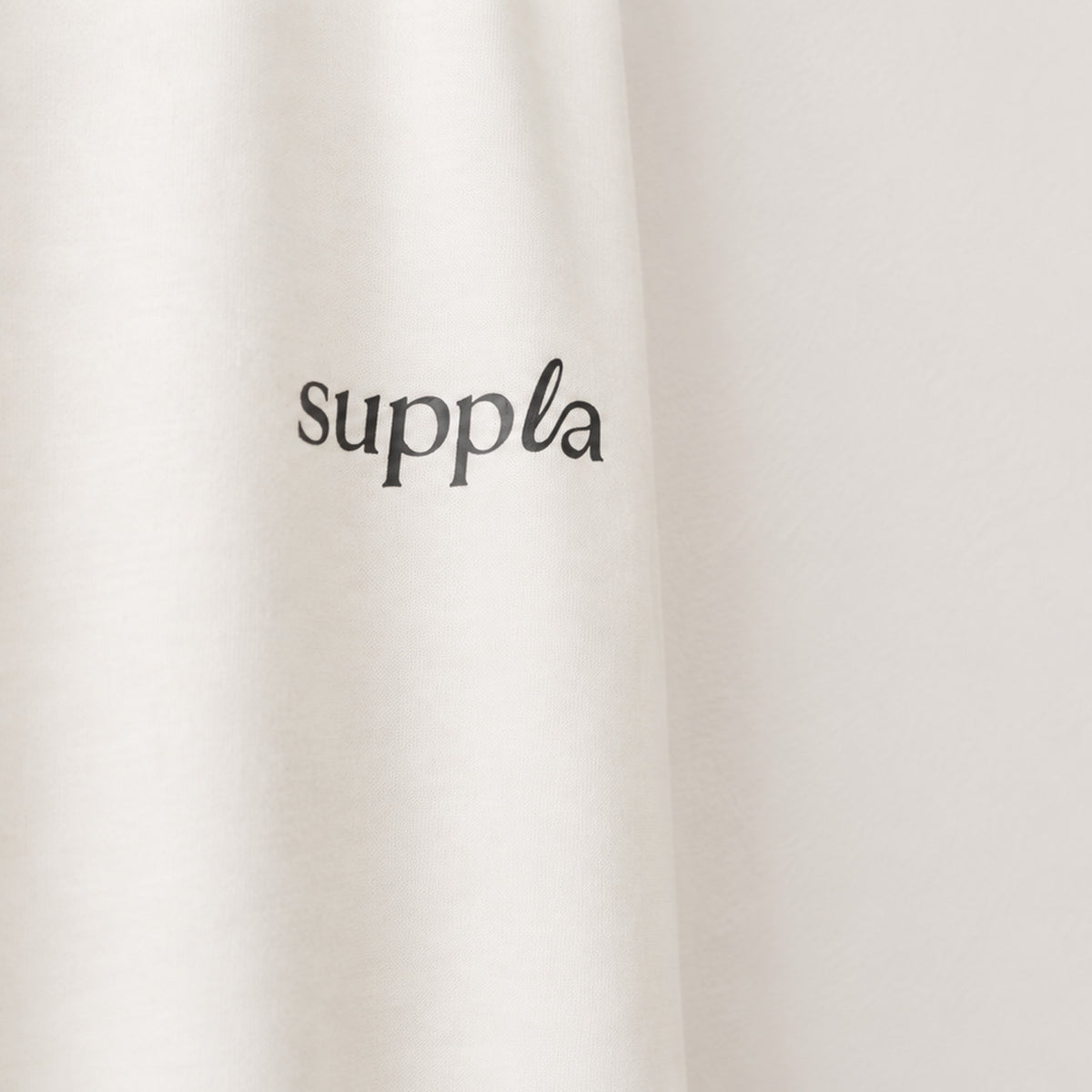 Close-up of a light cream or off-white fabric surface with the word 'suppla' printed in black script near the center.