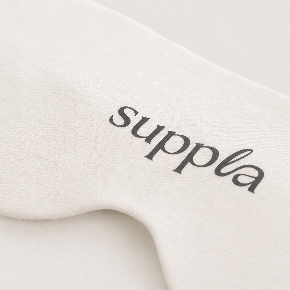 A close-up of a cream-colored sleepmask featuring the brand name 'suppla' printed in a black cursive font.