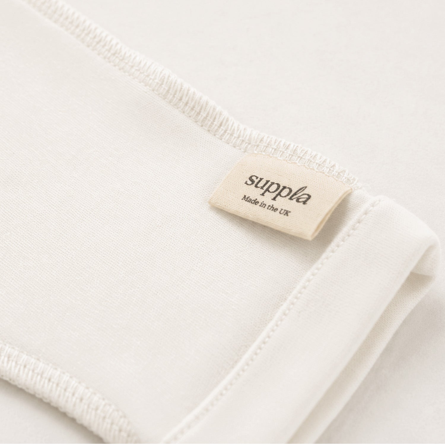 Close-up of a folded off-white scratch mitten with a small beige 'suppla Made in the UK' label near the hem.