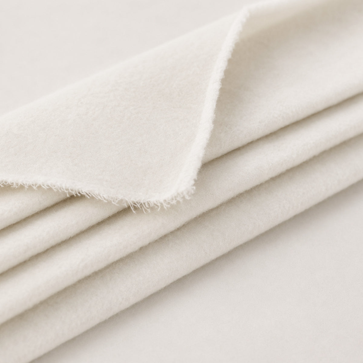 A close-up of folded off-white fabric with a soft, plush texture and a frayed edge, shown against a matching light background.