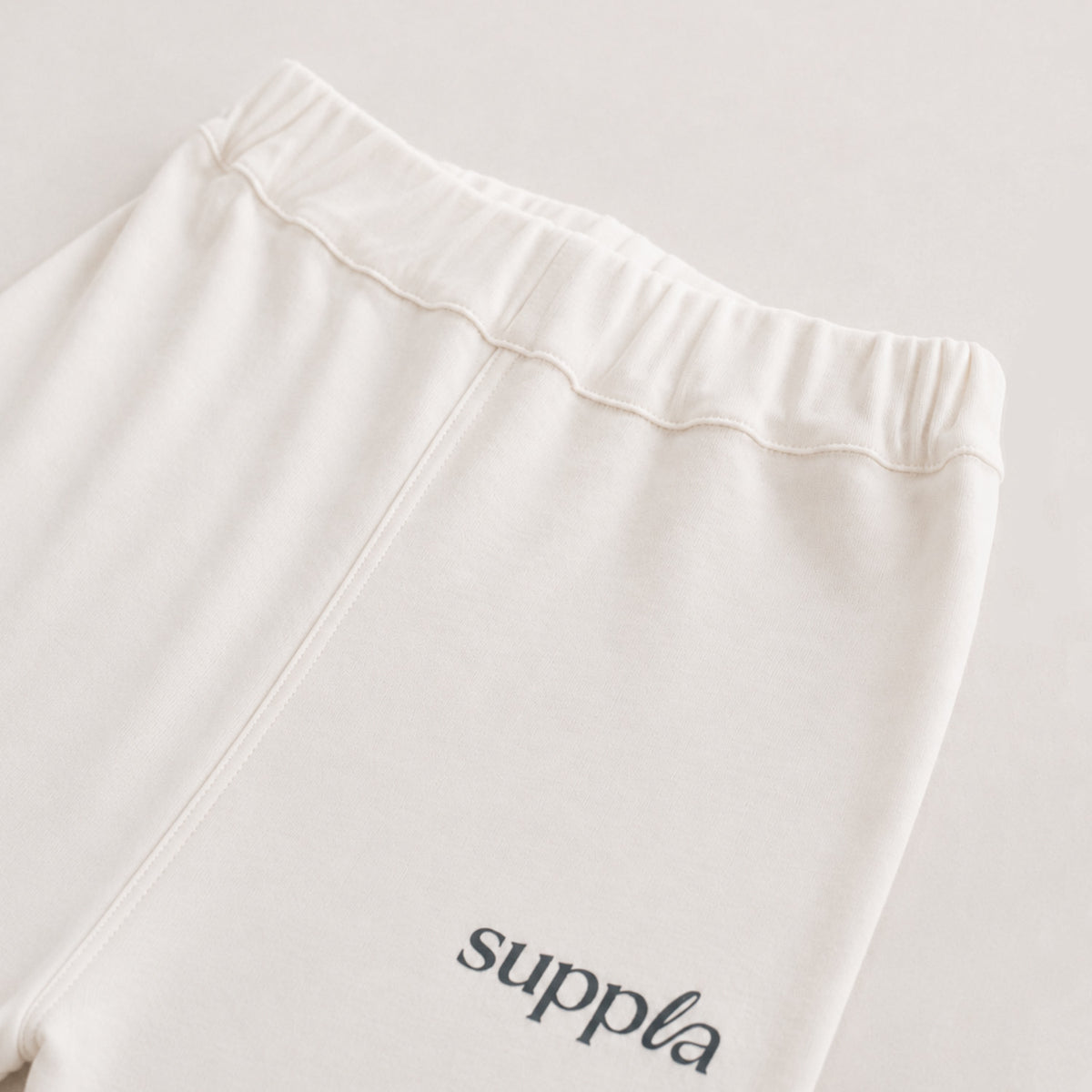 Close-up of a cream-colored eczema pyjama bottoms leg with an elastic waistband and the 'suppla' brand name printed in charcoal on the lower left leg.