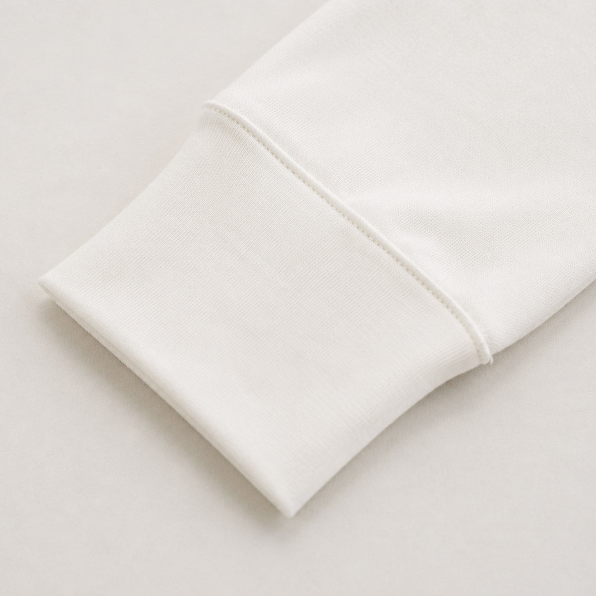 Close-up of a folded white knit fabric cuff from long sleeve top on a light neutral background.