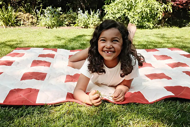 Girl smiling whilst lying on a red and white checkered blanket in a park or garden
