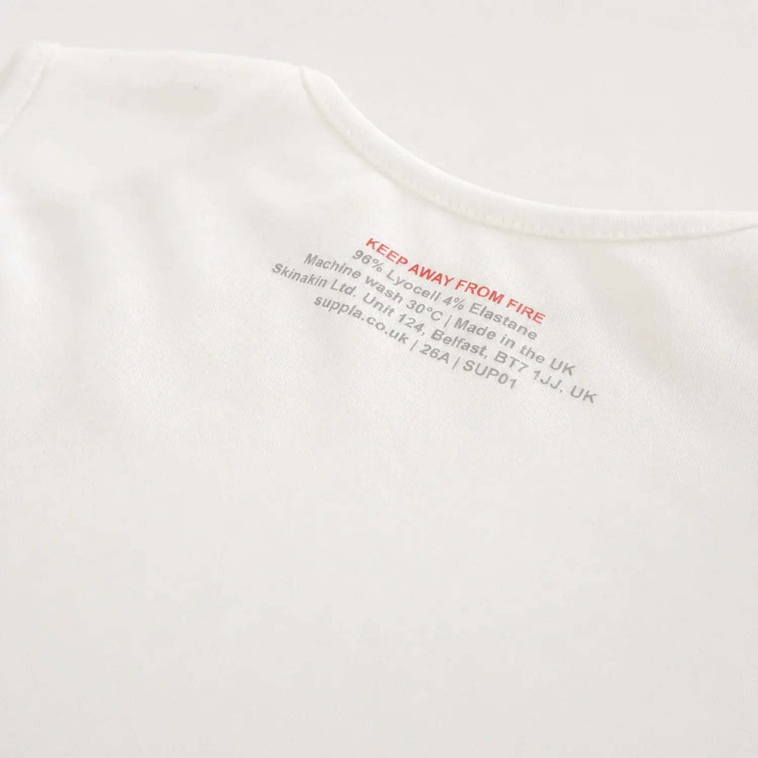 Close-up of a white t-shirt showing the externally printed care label with red and grey text details.