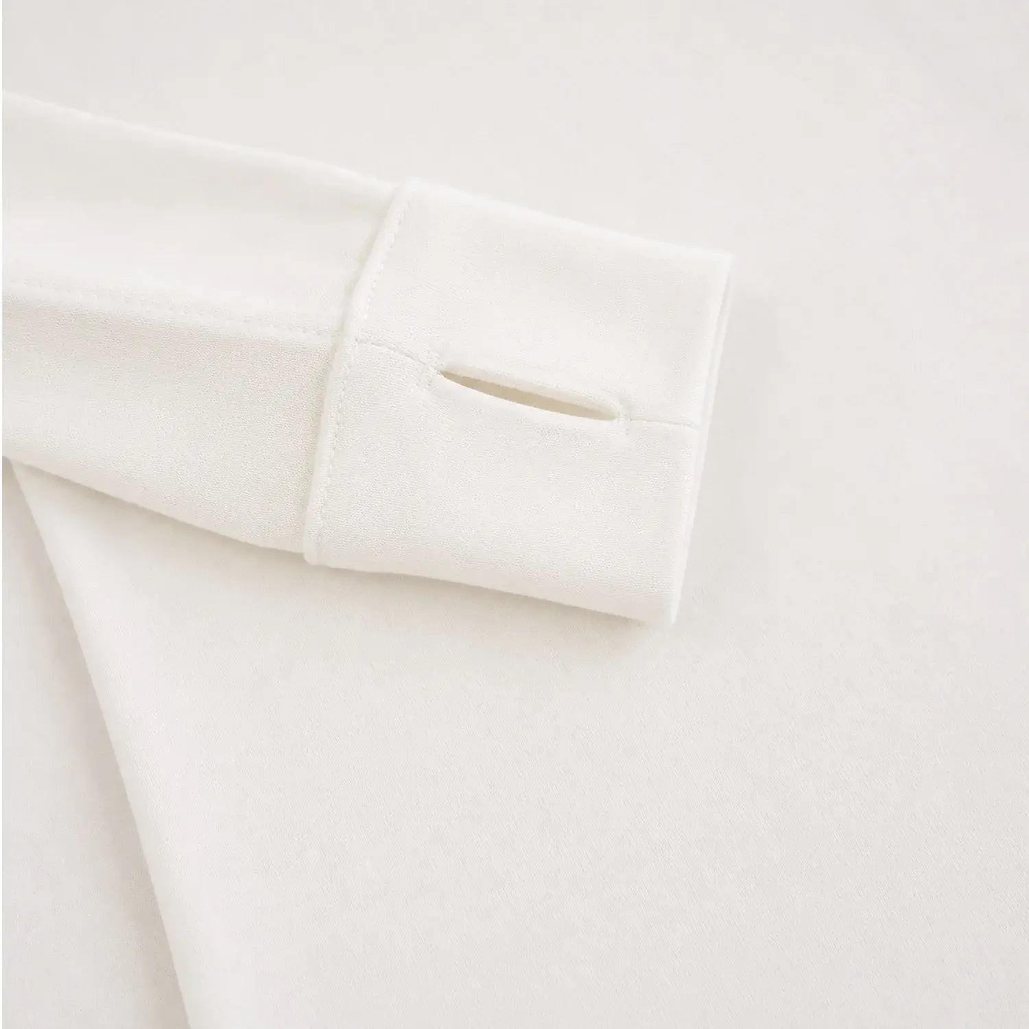 Close-up of a folded off-white fabric sleeve or cuff with thumbhole slit, shown on a matching light neutral background.