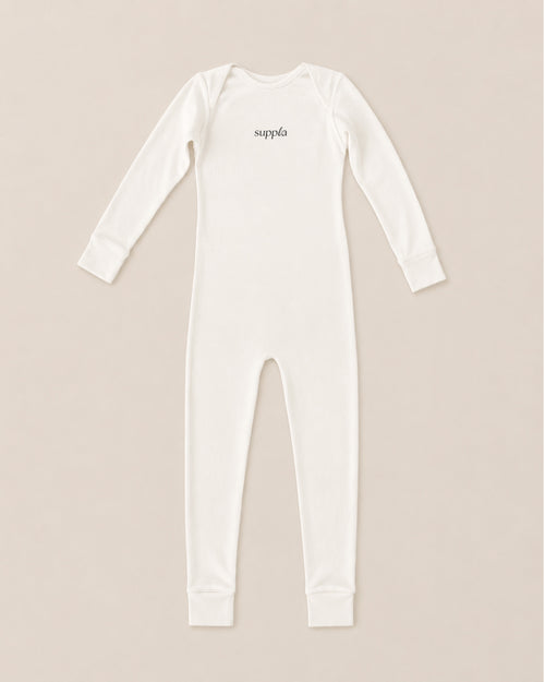 A long-sleeve eczema sleepsuit in off-white, featuring the brand name 'suppla' printed in black script on the chest, laid flat against a light beige background.