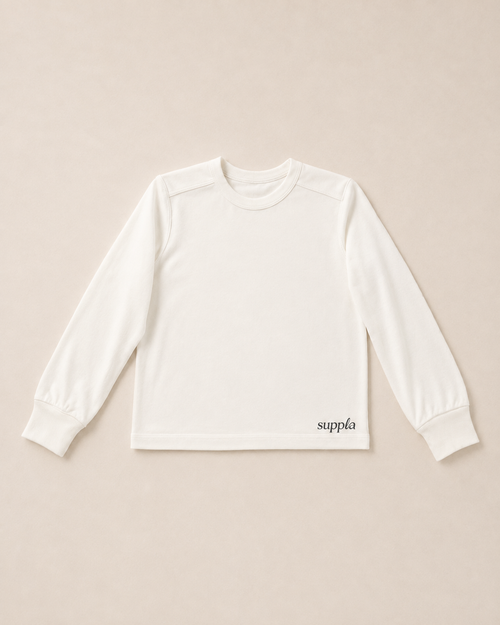 A white long-sleeve kids crewneck shirt with 'suppla' printed in black script near the bottom right hem, laid flat on a light beige background.