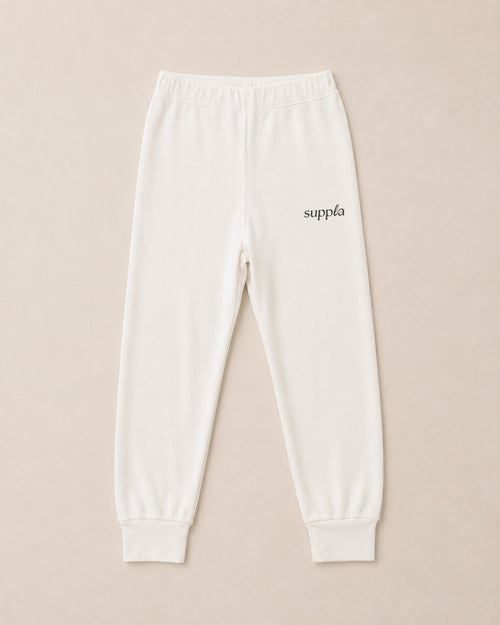 Off-white sweatpants with a small black 'suppla' logo on the left hip, displayed flat against a light beige background.