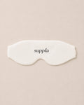 A white sleep mask with the brand name 'suppla' printed in black lowercase letters, centered on a solid beige background.