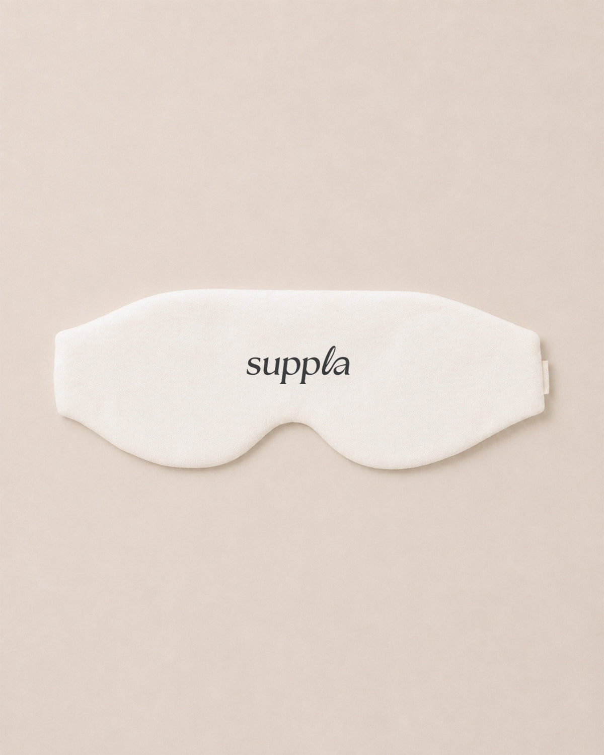 A white sleep mask with the brand name 'suppla' printed in black lowercase letters, centered on a solid beige background.