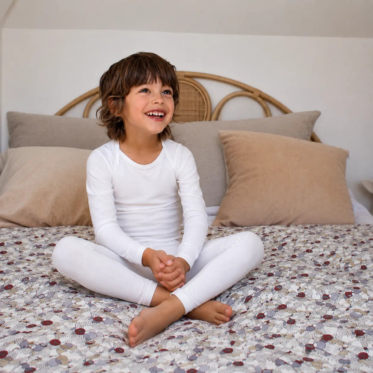 Child sitting on a bed wearing suppla calm eczema clothing with patterned bedding and beige pillows
