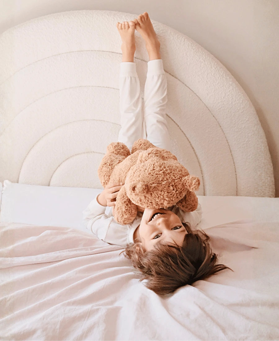 Child lying on a bed with a teddy bear, surrounded by soft bedding.
