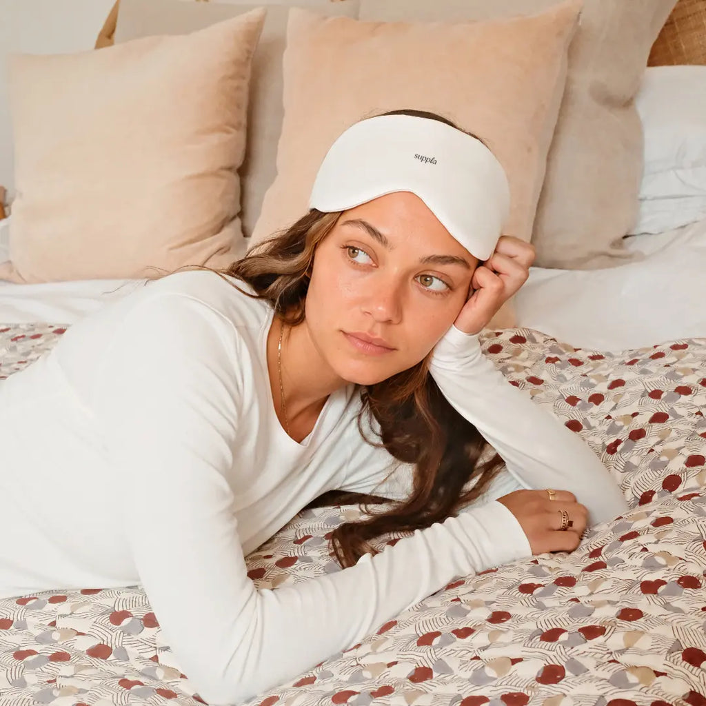 Girl wearing a Suppla sleep mask in bed with patterned bedding